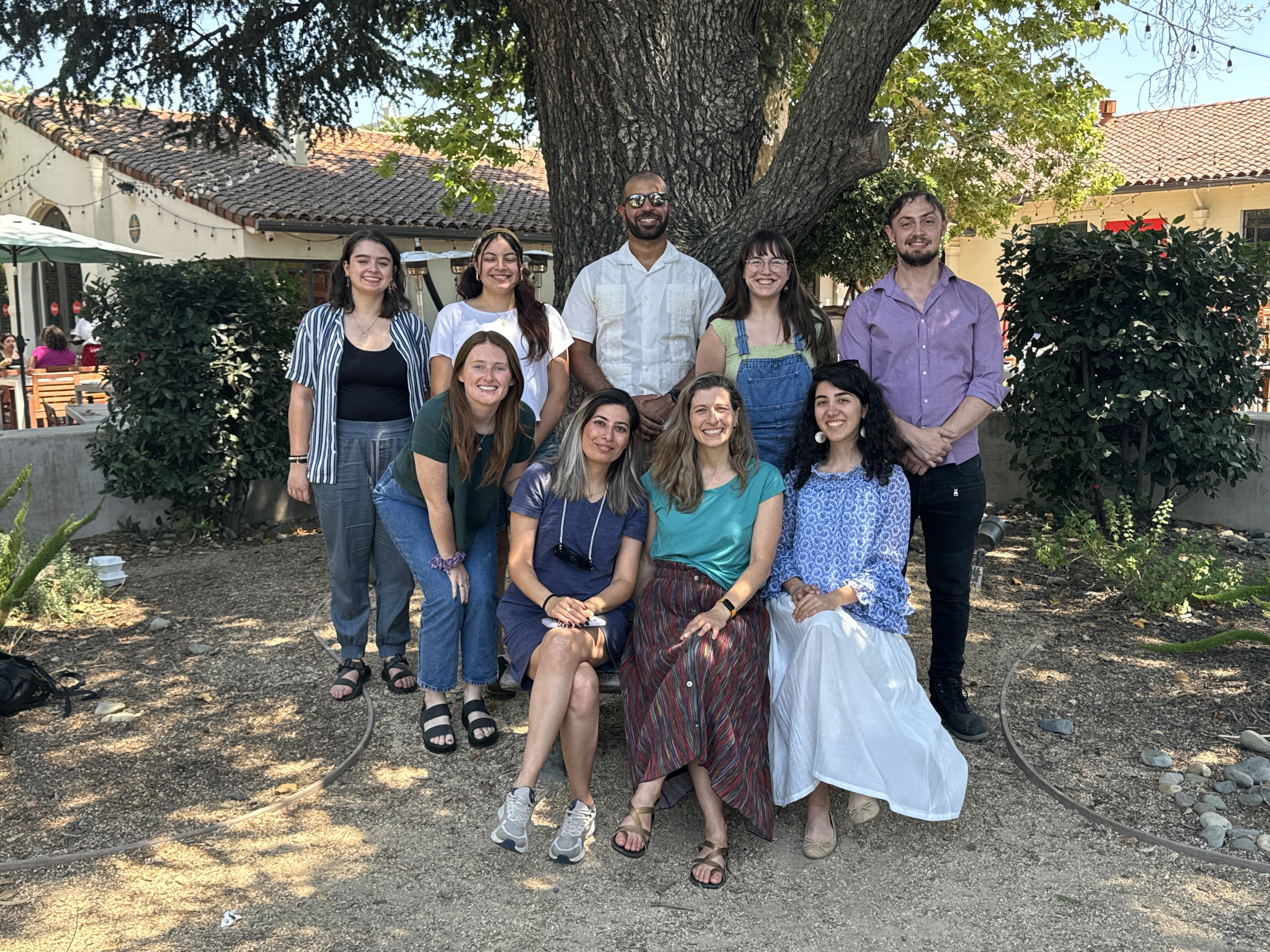 Group of CRD 250 students and instructor smiling under a large tree in a sunny courtyard.